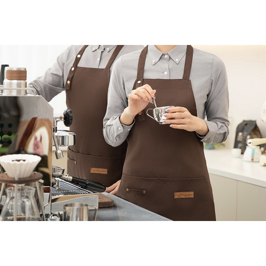 Brown apron with buttoned neck strap and front pocket worn by person holding a small metal cup