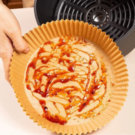 Brown ridged nonstick air fryer paper liner with oil and sauce stains held by hand