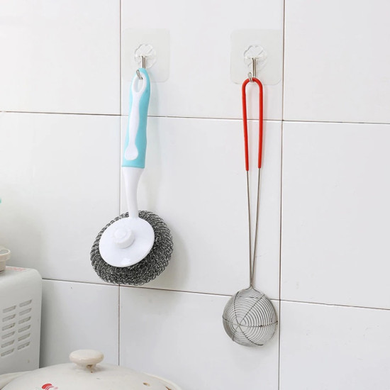 Two clear adhesive wall hooks holding a kitchen scrubber with blue handle and a metal skimmer with red handle