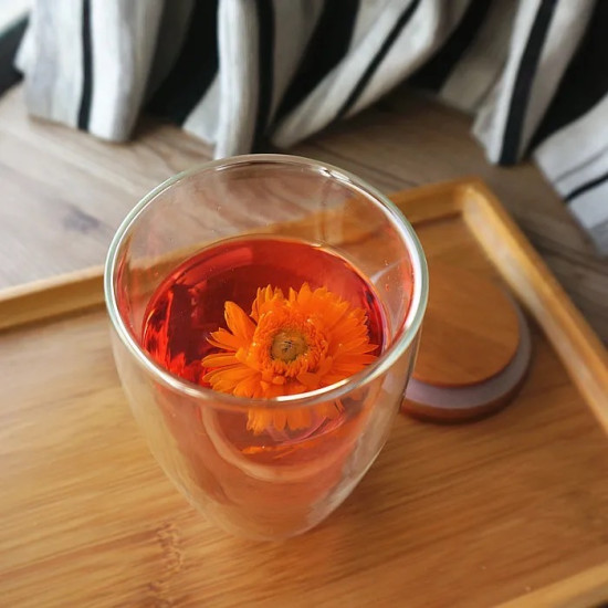 Clear Double Wall Glass Cup with Bamboo Lid and Orange Flower Tea Clear double wall glass cup with bamboo lid and orange flower tea inside on wooden tray