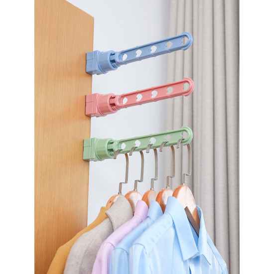 Colorful wall-mounted folding hooks with heart-shaped holes holding clothes Three wall-mounted folding hooks in blue, pink, and green attached to a wooden surface. Each hook arm has five heart-shaped holes. The green hook holds six wooden hangers with clothes including beige, purple, and blue shirts.