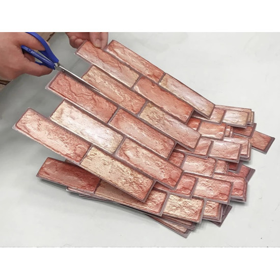 Hands cutting self-adhesive 3D foam wall panels with red brick pattern
