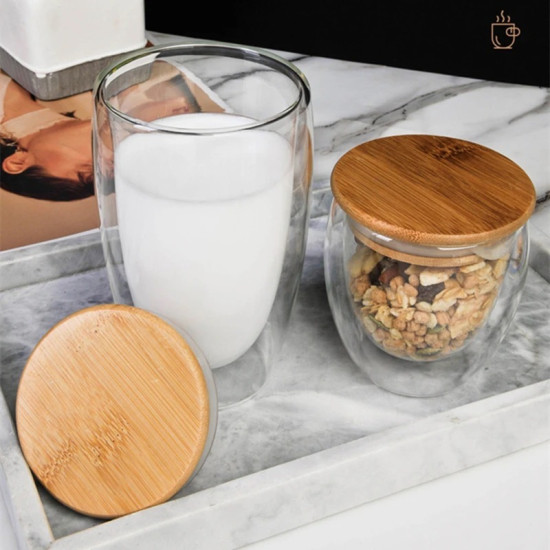 Double Wall Glass Cup and Jar with Bamboo Lids on Marble Tray Double wall glass cup filled with milk and jar with cereal, both with round bamboo lids on a marble tray