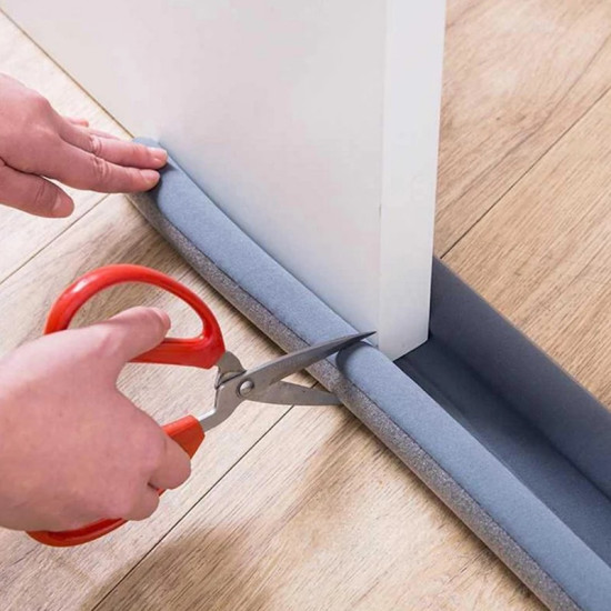 Dust and Insect Door Bottom Seal - Air and Dirt Insulator Without Drilling Cutting gray foam door bottom seal with scissors on wooden floor to block air and insects