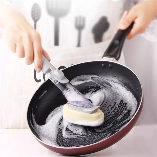 Dish Cleaning Brush with Gray Soap Container and White Sponge Head Hand holding a gray soap container dish cleaning brush with a white sponge head scrubbing a black frying pan with soap foam inside.