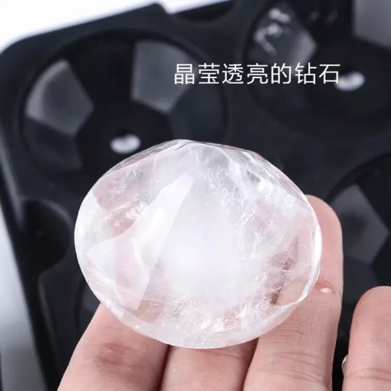 Clear Faceted Large Ice Cube with Black Mold Hand holding a clear faceted large ice cube in front of a black ice cube mold with multiple diamond-shaped cavities