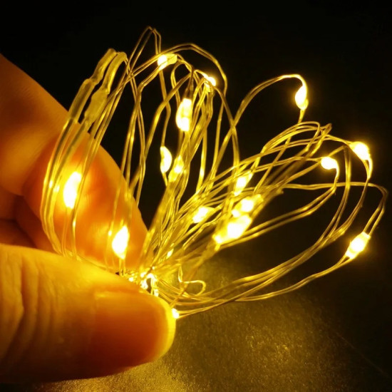 شريط إضاءة LED أصفر لتزيين الغرف والمكاتب يد تمسك شريط إضاءة LED أصفر متوهج بأسلاك فضية رفيعة