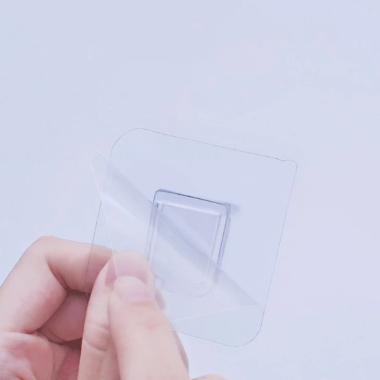 Hand peeling protective film from a transparent adhesive shelf bracket with square base