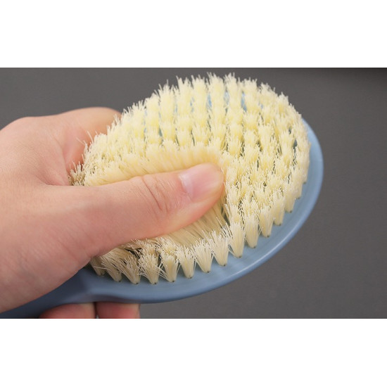 Hand pressing soft white bristles of a blue body brush for back massage and cleaning