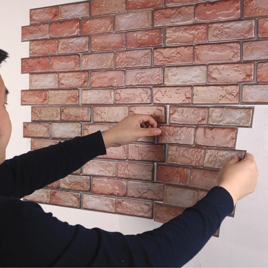 Hands applying self-adhesive 3D foam wall panels with red and beige brick pattern
