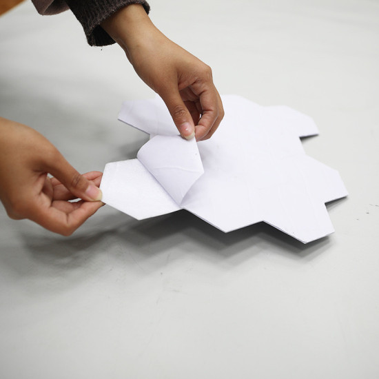 Hands peeling adhesive backing from a white hexagonal self-adhesive foam wall panel