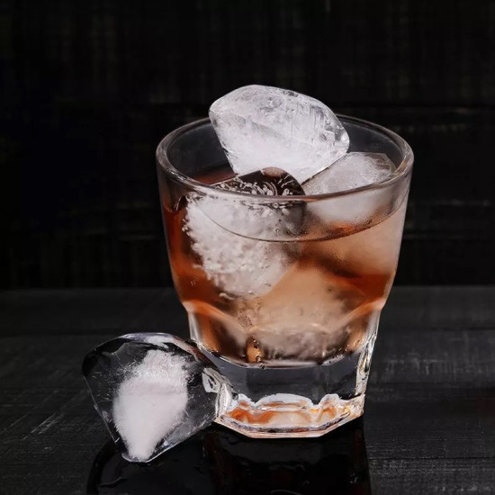 Large Clear Faceted Ice Cubes in Glass with Amber Drink Large clear faceted ice cubes inside a glass filled with amber liquid and one ice cube placed outside the glass on a black surface