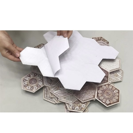 Hand peeling adhesive backing from textured hexagonal foam wall panels with beige and brown decorative patterns