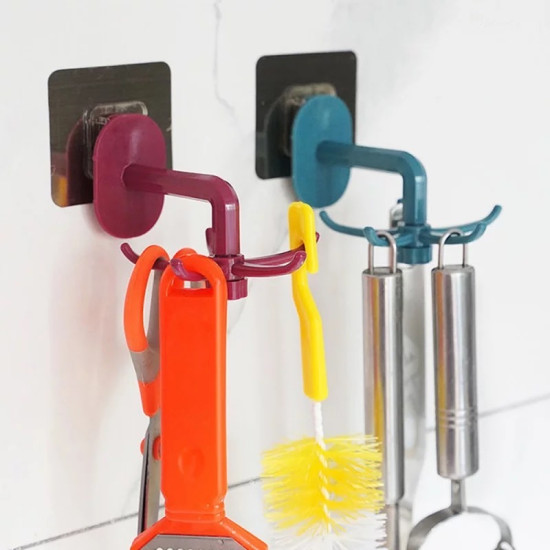 Two rotating hooks mounted on a white tiled wall with adhesive black square bases. The left hook is maroon with four curved arms holding orange scissors and an orange brush with a handle. The right hook is teal with four curved arms holding two stainless 