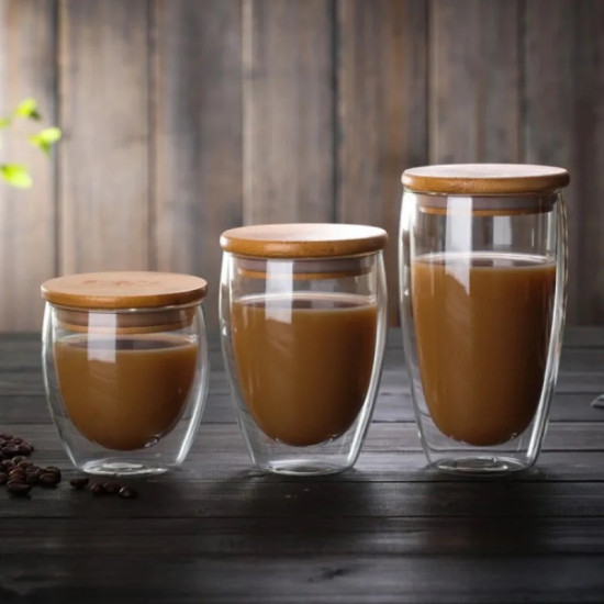 Double Wall Glass Cups with Bamboo Lids for Hot Drinks Three double wall glass cups filled with coffee and topped with flat bamboo lids on a dark wooden surface
