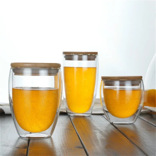 Double Wall Glass Cups with Bamboo Lids for Beverage Heat Retention Three double wall glass cups filled with orange liquid, each with a flat bamboo lid on top