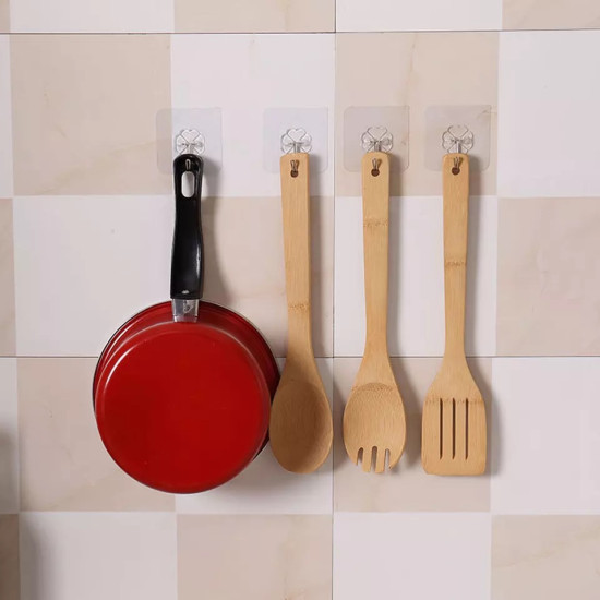 Transparent adhesive hooks holding a red frying pan and three wooden kitchen utensils on tiled wall