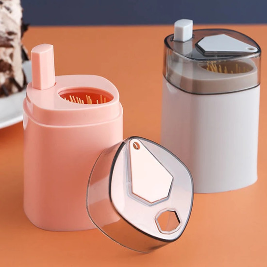 elegant-automatic-toothpick-boxes-with-transparent-lids Two automatic toothpick dispensers, one pink and one white, both with transparent lids. The pink dispenser has a rectangular button on the top left side and visible toothpicks inside. The white dispenser has a similar rectangular button and a transparent