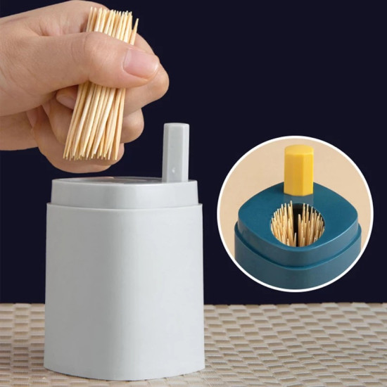 Elegant Automatic Toothpick Dispenser Box with 100 Toothpicks Capacity A white automatic toothpick dispenser with a vertical rectangular button on the top right side. A hand is holding a bundle of toothpicks above the dispenser. The inset shows a close-up of a blue dispenser top with a yellow rectangular button and toothpick