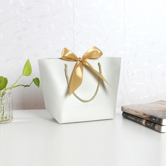 White Paper Gift Bag with Golden Ribbon Bow White paper gift bag with twisted rope handles and a golden satin ribbon bow on top
