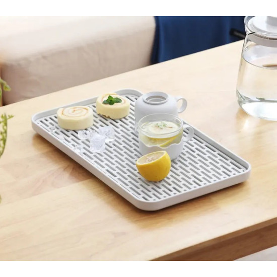Double-layer spill-proof serving tray with slotted surface White rectangular serving tray with slotted draining surface holding a cup of lemon water and two pastries