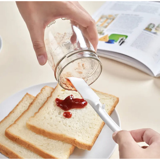 White silicone spatula scraping red jam from a glass jar onto bread slices on a white plate